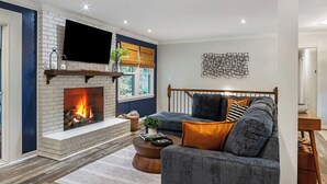 A living room with a fireplace, a sofa, a coffee table, and a wall-mounted TV. - Pool Table + Hot Tub - Raleigh Retreat (Raleigh)