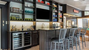 A modern kitchen with a central island, bar stools, and a variety of decorative items on shelves. - Pool Table + Hot Tub - Raleigh Retreat (Raleigh)