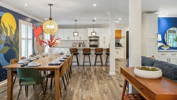 A modern kitchen with white cabinets, a dining area with wooden tables and chairs, and a living room with a sofa and a decorative bowl. - Pool Table + Hot Tub - Raleigh Retreat (Raleigh)
