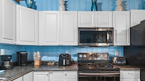 A kitchen with white cabinets, a microwave, a toaster, a coffee maker, and a stove.