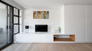 A modern living room with a flat-screen TV, a painting, and a small plant on a white console table. - One Bedroom | Green Point | Spacious (Cape Town)