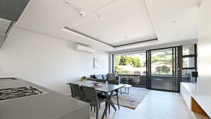 A modern kitchen with a central island, dining area with a table and chairs, and a large sliding glass door leading to an outdoor patio. - One Bedroom | Green Point | Spacious (Cape Town)