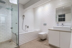 Ein modernes Badezimmer mit weißen U-Bahn-Fliesen, einer Glasduschkabine, einer weißen Badewanne, einer Toilette und einem Waschbecken mit Spiegel darüber.