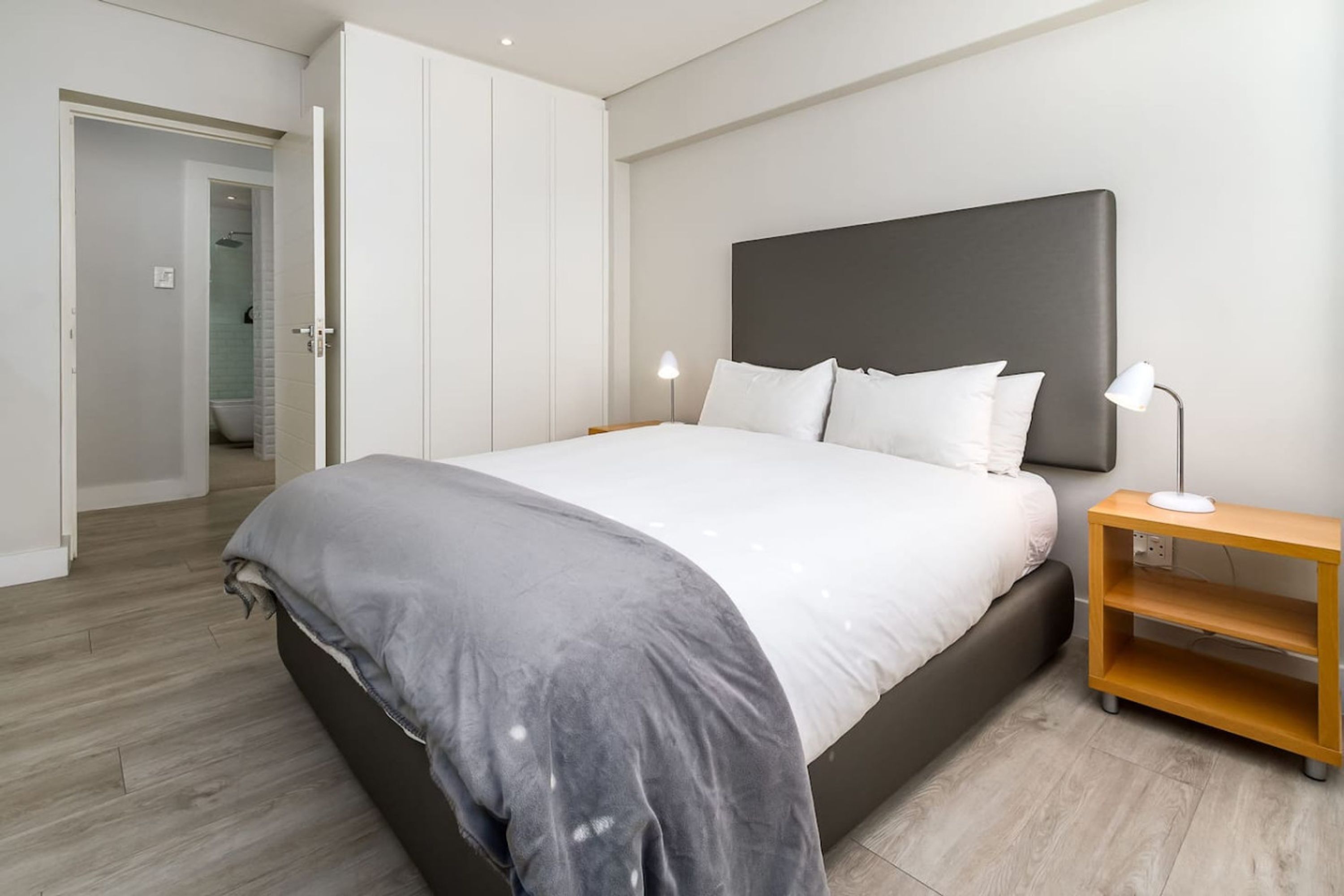 Une chambre à coucher moderne avec un grand lit, une table de chevet avec une lampe et une armoire.