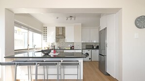 Eine moderne Küche mit weißen Schränken, einem Edelstahlkühlschrank, einem Einbauofen und einer großen Kochinsel mit Barhocker.