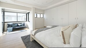 Ein modernes Schlafzimmer mit einem großen Bett, einem eingebauten Kleiderschrank und einer Sitzecke mit Blick ins Freie.