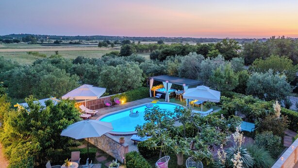 Une piscine entourée d’espaces de détente et de parasols, située dans un jardin luxuriant avec vue sur la campagne.