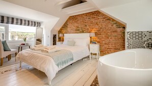 Een slaapkamer met een groot bed, een witte badkuip, een bakstenen muur en uitzicht op het platteland.