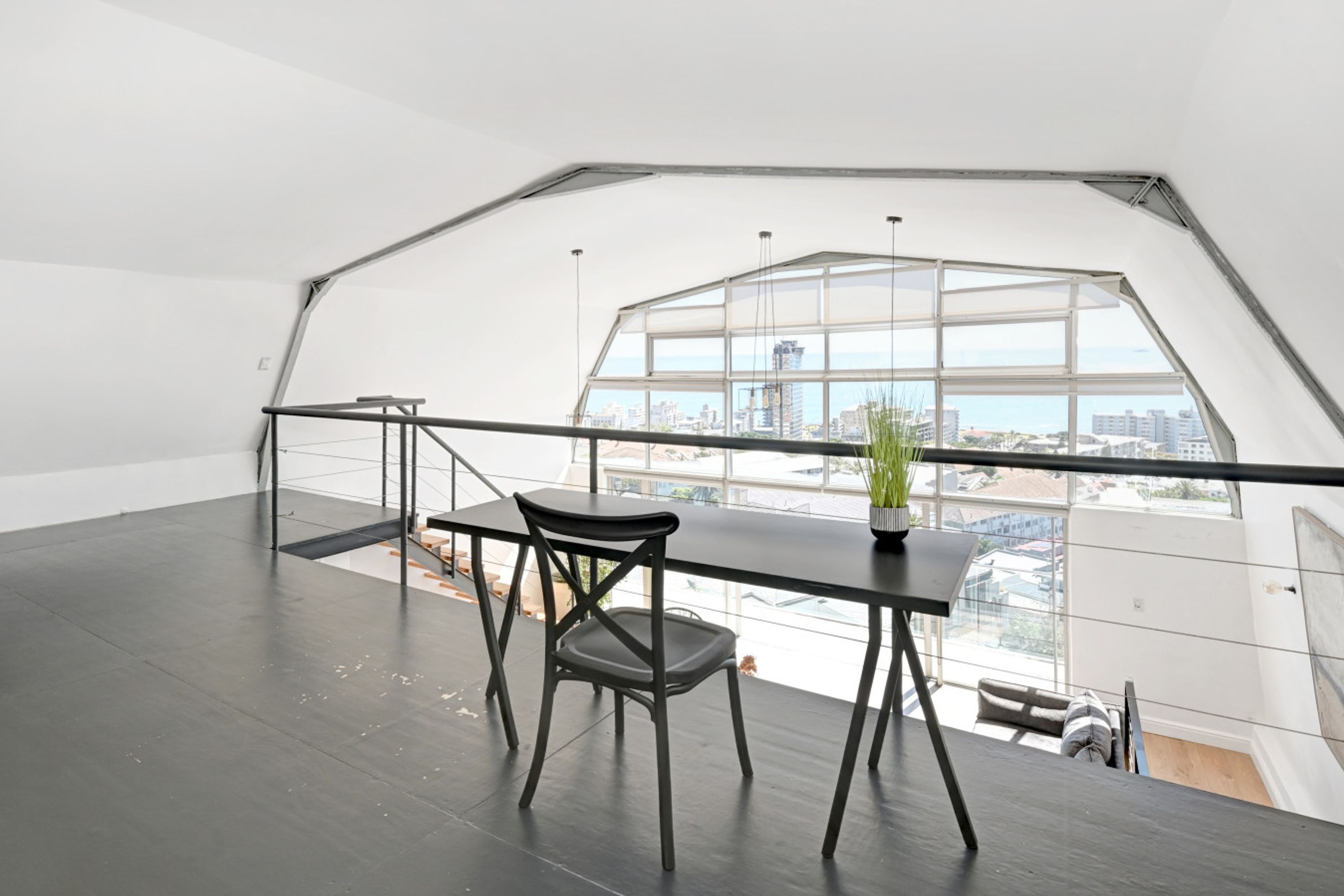 A spacious loft with a large skylight, a black table with a chair, and a potted plant.