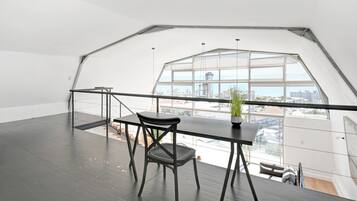 A spacious loft with a large skylight, a black table with a chair, and a potted plant.