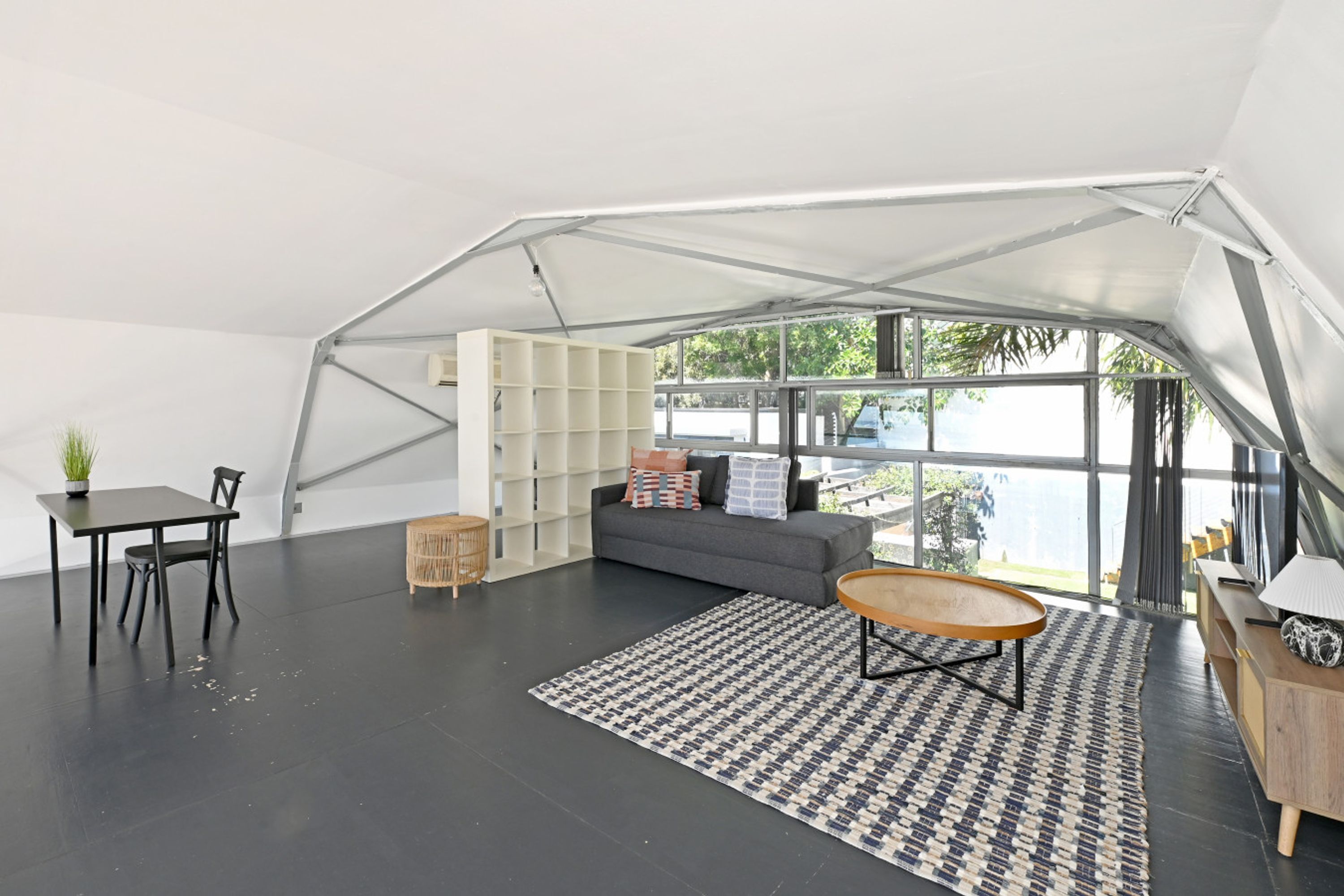 A spacious, modern interior with a large window, a sofa, a dining table, and a patterned rug.