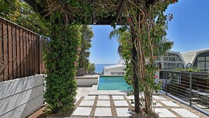 Zwembadgedeelte met een pergola, een pad van stenen en uitzicht op zee.