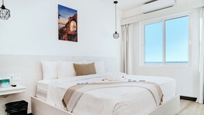 Quarto de hotel moderno com uma cama grande, mesa de cabeceira com abajur, pintura na parede e uma janela com cortinas.