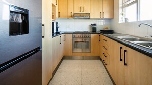 Eine kompakte Küche mit Holzausstattung, einem Edelstahlkühlschrank und einem eingebauten Backofen.