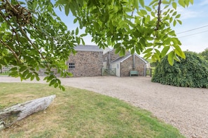 A stone building with a gravel driveway, surrounded by greenery and a wooden log.