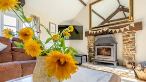 A living room with a stone fireplace, a brown leather sofa, a marble coffee table, and a vase of sunflowers. - 3 Bed in Fairy Cross (oc-g32972) (Ford)