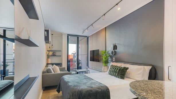 Un dormitorio moderno con cama, un pequeño sofá, un televisor y un comedor.