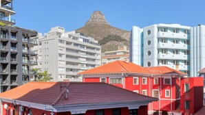 Un edificio moderno con balcones y techo rojo, rodeado de otros edificios de diversos estilos arquitectónicos.