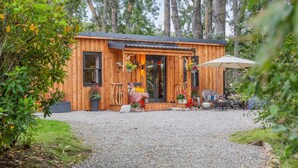 A wooden cabin with a gravel driveway, surrounded by trees. - 2 Bed in Invergordon (oc-c33073) (Invergordon)