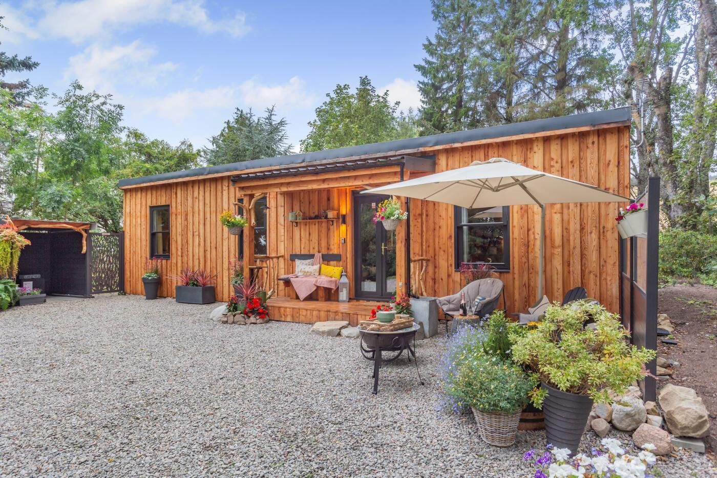 A wooden cabin with a covered porch, outdoor seating, and potted plants.