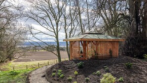 A gazebo with a wooden lattice structure, surrounded by a landscaped garden with various plants and a gravel path. - 2 Bed in Invergordon (oc-c33073) (Invergordon)