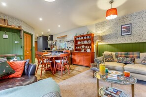A cozy living room with a sofa, a dining table with chairs, a kitchen area with a cabinet, and a patterned wall.