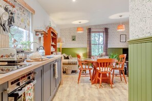 A kitchen with a wooden countertop, a dining area with orange chairs, and a green wall.