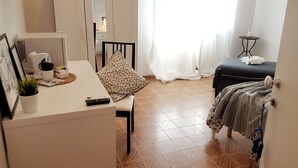 A hotel room with a bed, a desk with a chair, a small table with a plant, a remote control, and a window with curtains. - B & B CELESTE BEDONIA 5 minutes from town center (Bedonia)