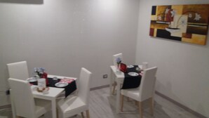 A dining area with two white tables, each set with plates, glasses, and a red napkin. The room has white walls and a painting on the wall. - B & B CELESTE BEDONIA 5 minutes from town center (Bedonia)