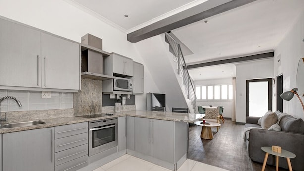 A modern kitchen with grey cabinets, a built-in microwave, and a large island. - Secure Sea Point | Spacious | Three Bedroom house (Cape Town)