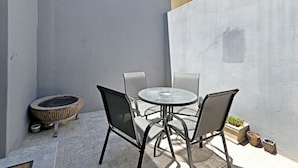 A small outdoor patio with a round table and four chairs, a small round table with a woven edge, and two potted plants. - Secure Sea Point | Spacious | Three Bedroom house (Cape Town)
