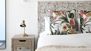 A neatly made bed with floral pillows, a bedside lamp, and a wooden nightstand. - Secure Sea Point | Spacious | Three Bedroom house (Cape Town)