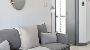 A modern living room with a grey sofa, a round mirror, and a floor lamp. - Secure Sea Point | Spacious | Three Bedroom house (Cape Town)