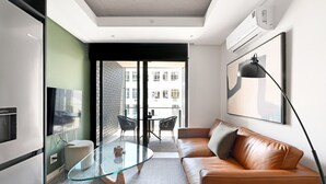 A modern living room with a glass coffee table, leather sofa, and a large window offering a view of buildings. - Station house | Studio Apartment | Gym |Rooftop Pool (Cape Town)