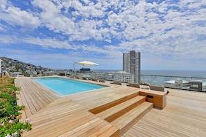 Ein Pool auf dem Dach mit Holzboden und Blick auf Stadt und Meer.
