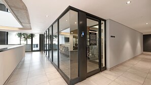 A modern hotel lobby with glass doors leading to a fitness area. - Station house | Studio Apartment | Gym |Rooftop Pool (Cape Town)