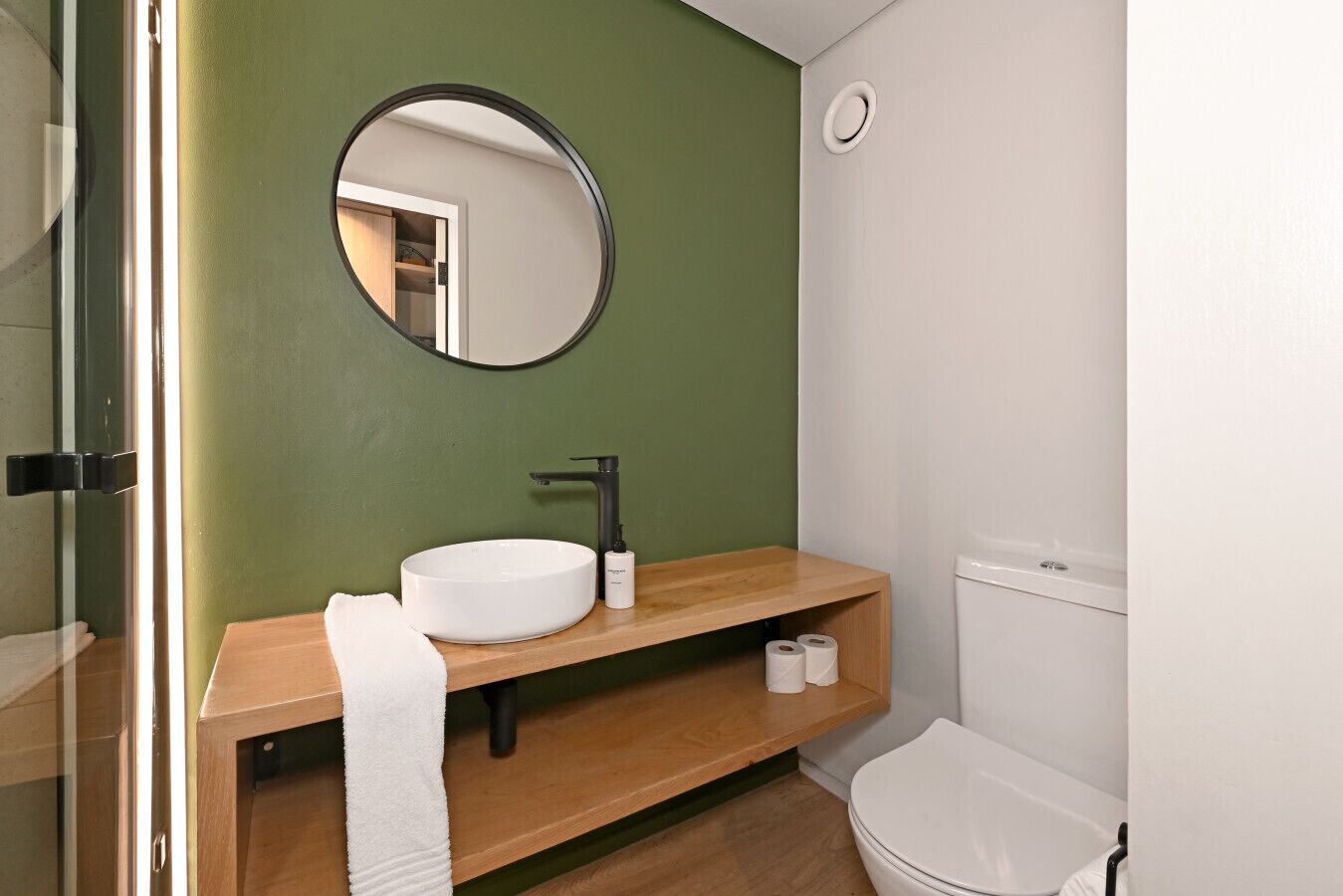 A bathroom with a round mirror, a white sink, a wooden vanity, and a toilet.