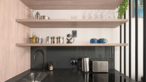 Cocina moderna con encimera negra, pileta de acero inoxidable y horno integrado. Se observan estantes sobre la encimera con diversos utensilios de cocina.