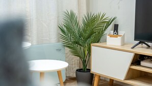 Un salon moderne avec une table ronde blanche, une plante en pot, un meuble TV en bois et une télécommande.