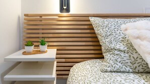 Une chambre à coucher moderne avec une tête de lit en lattes de bois, une table de chevet agrémentée de deux plantes en pot et une couvre-lit à motifs.