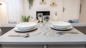 Une table à manger dressée avec des assiettes, des verres et des couverts, avec une télévision et des plantes en arrière-plan.