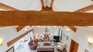 Amplia sala de estar con techo alto, vigas de madera a la vista, un candelabro, chimenea y televisor.