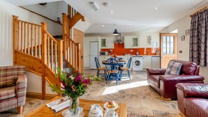 A spacious living area with a wooden staircase, a dining table with chairs, a sofa, and a kitchen in the background. - 2 Bed in Ponthirwaun (oc-c33293) (Ponthirwaun)