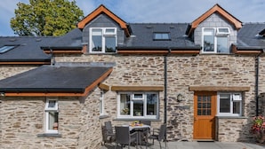 A stone house with a tiled roof, a wooden door, and a patio with outdoor furniture. - 2 Bed in Ponthirwaun (oc-c33293) (Ponthirwaun)