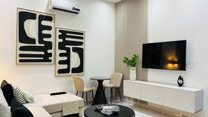 A modern living room with a sofa, two chairs, a coffee table, a TV, and a white console. - Cozy Elegant Condo 1BR Apartment (Adenta Municipality)