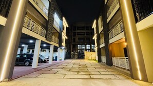 A multi-story building with a central courtyard, featuring a covered parking area with cars and a decorative gate. - Cozy Elegant Condo 1BR Apartment (Adenta Municipality)