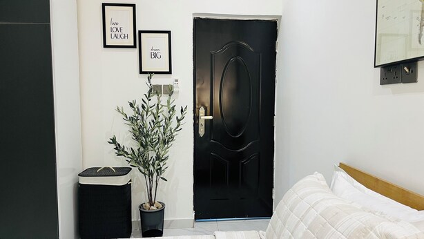 Een slaapkamer met een zwarte deur, een kamerplant, een bed en twee ingelijste motiverende citaten aan de muur.