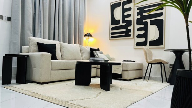A modern living room with a sofa, a coffee table, a side table, a lamp, and a chair. - Cozy Elegant Condo 1BR Apartment (Adenta Municipality)