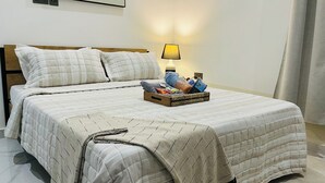 A neatly made bed with a quilted bedspread, two pillows, a bedside lamp, and a basket of toiletries on the nightstand. - Cozy Elegant Condo 1BR Apartment (Adenta Municipality)
