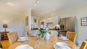 A dining area with a wooden table set for six, surrounded by wooden chairs. A vase with flowers is placed in the center. - 3 Bed in Fowey (oc-o33078) (Fowey)
